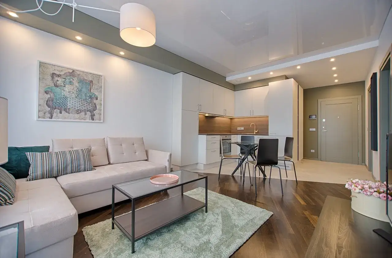 En modern l&auml;genhet med en bekv&auml;m soffa, k&ouml;k och matplats. En taklampa ger ett varmt, vitt ljus &ouml;ver rummet.