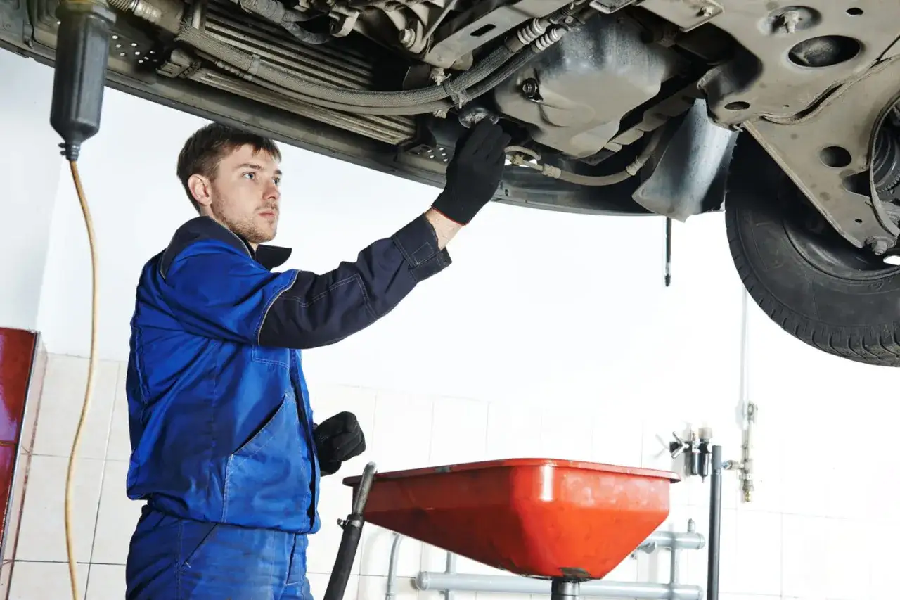 Mécanicien effectuant la vidange d'une voiture diesel, récupérant l'huile usagée dans un bac rouge.
