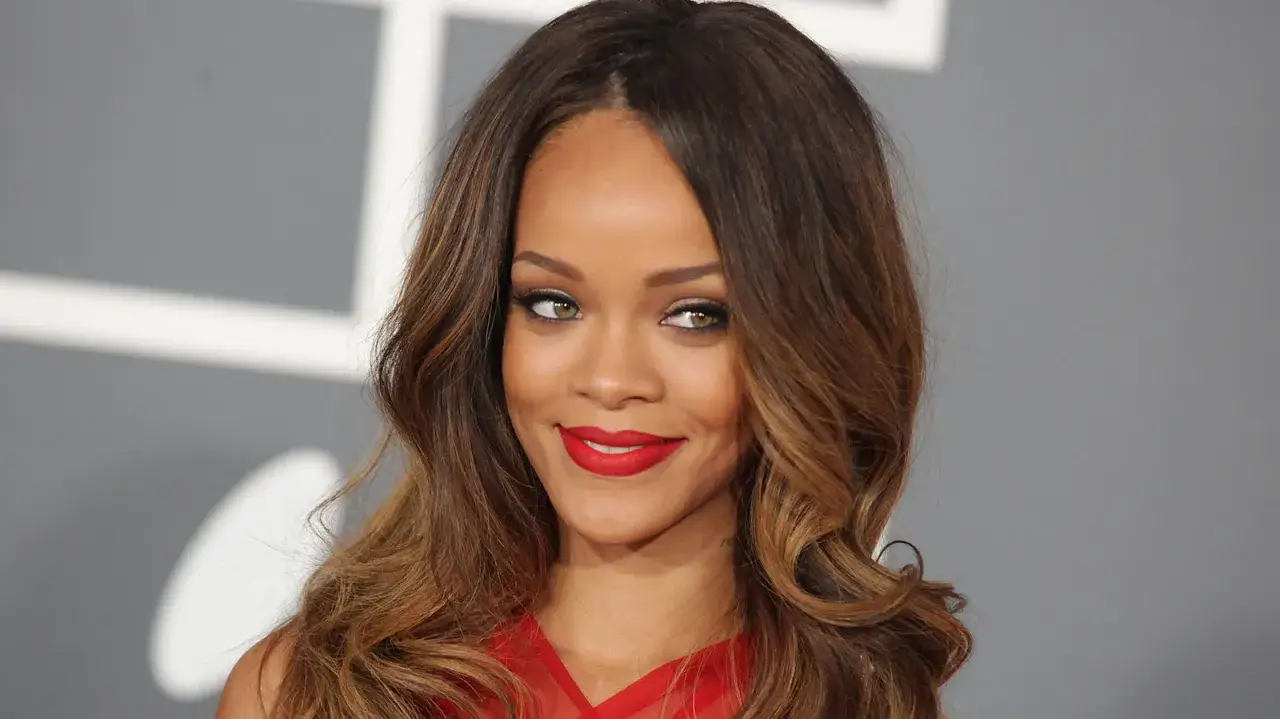 Rihanna z burzą brązowych loków i wyrazistym makijażem, podkreślającym jej wysokie czoło i zielone oczy.