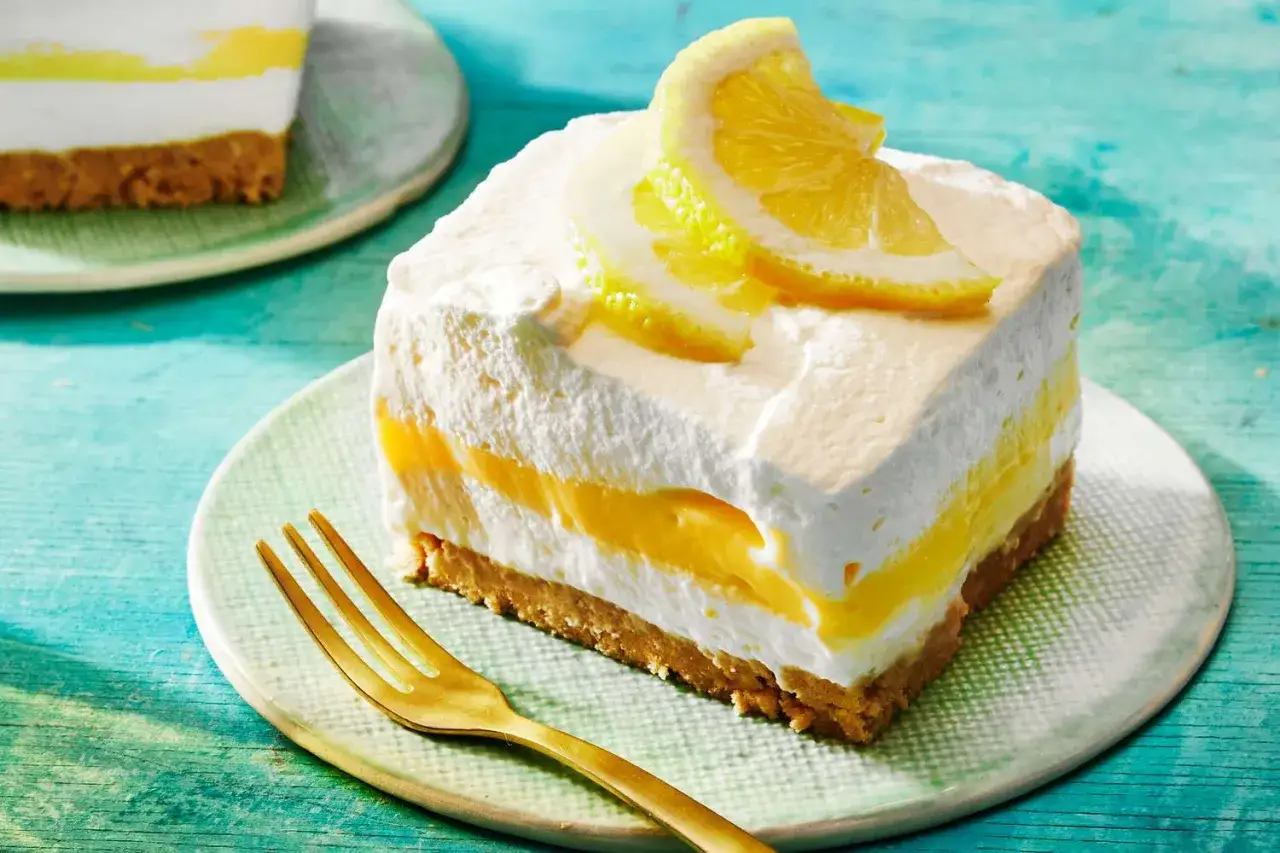 En bit krämig dessert med lager av fluffig grädde och syrlig lemon curd, toppad med citronskivor. En gyllene gaffel ligger bredvid.