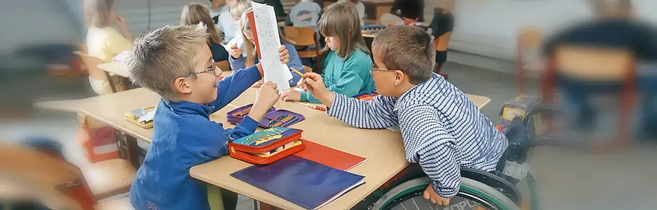 Zwei Jungen lernen gemeinsam, einer im Rollstuhl. Ein Beispiel f&uuml;r gelungene **Inklusion an Schulen**, wo jeder dazugeh&ouml;rt und unterst&uuml;tzt wird.