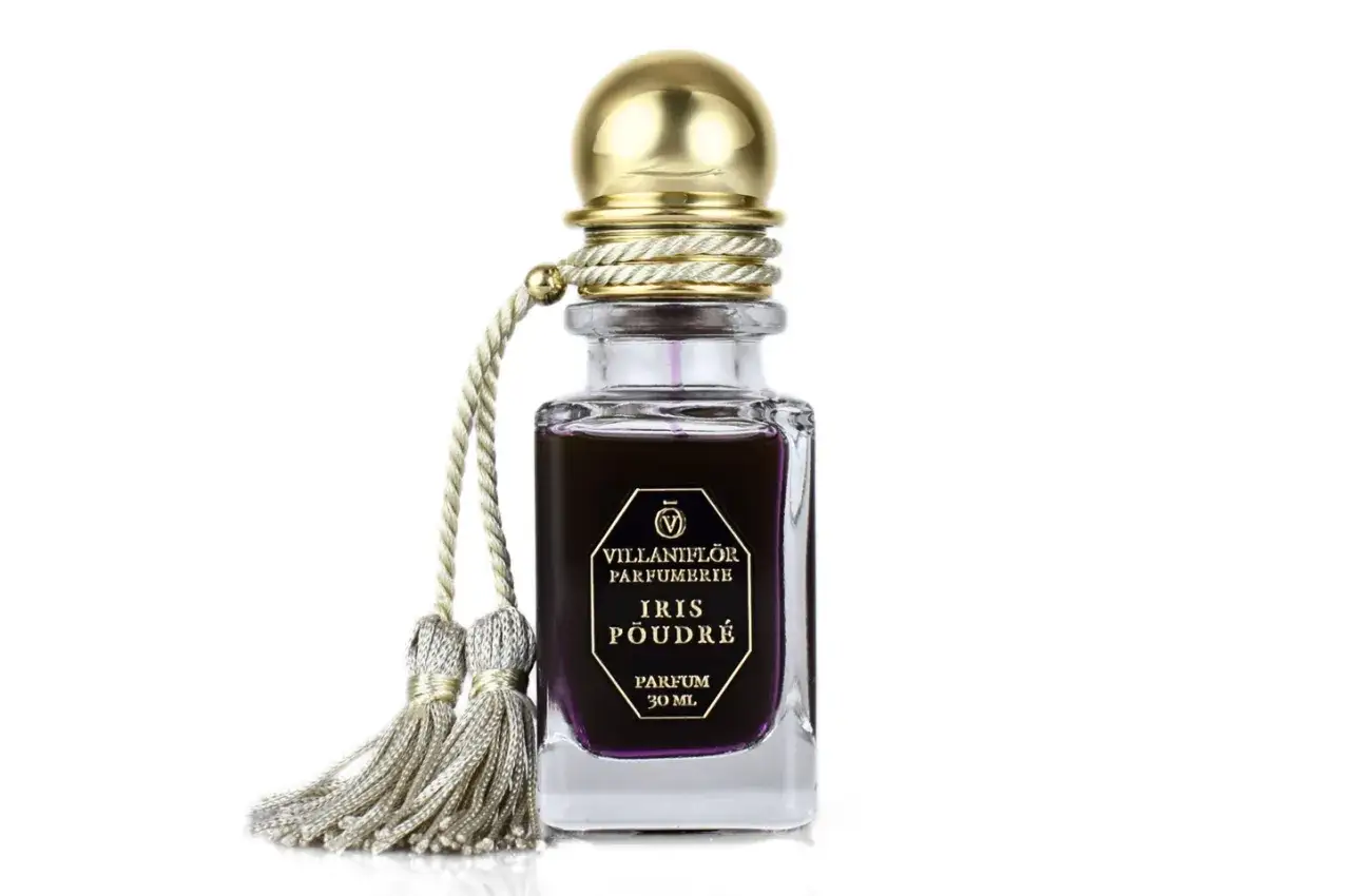 Elegancka buteleczka perfum Iris Poudré z ozdobnym złotym korkiem i frędzlami.