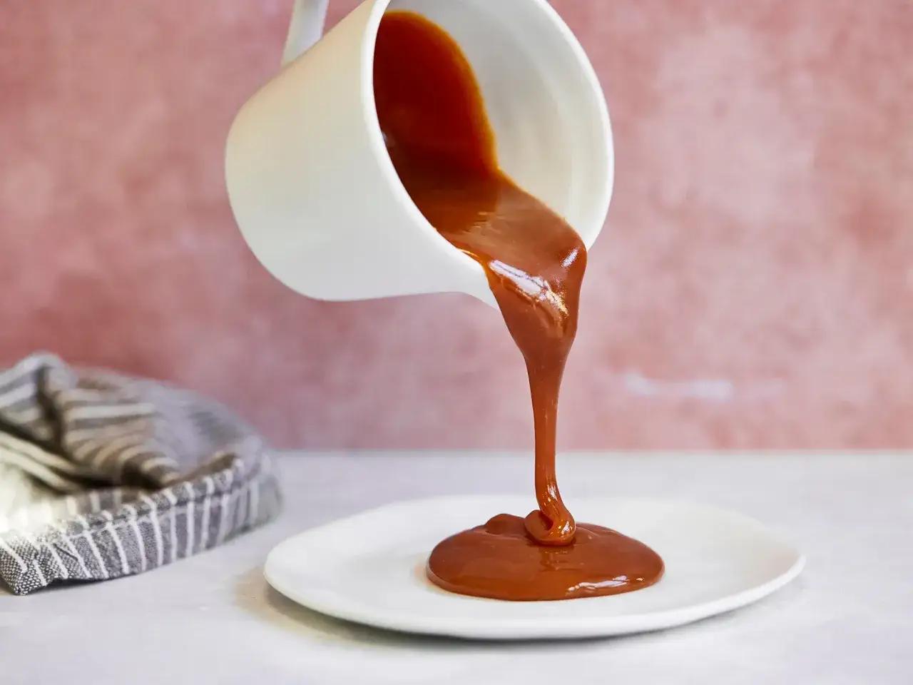 Flüssige Karamellsauce fließt aus einer weißen Kanne auf einen Teller. Ein einfaches karamellsauce rezept für süße Momente.