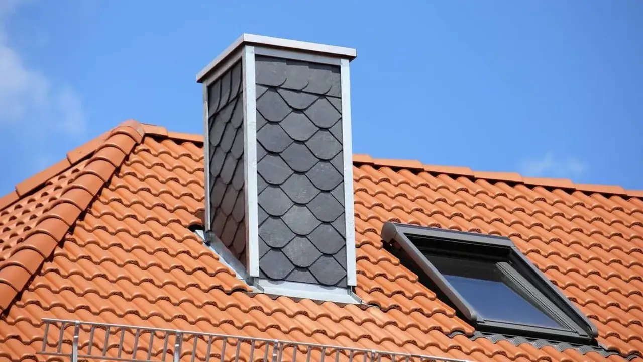 Moderner gemauerter Schornstein verkleidet mit dunklen Schindeln auf einem Ziegeldach.