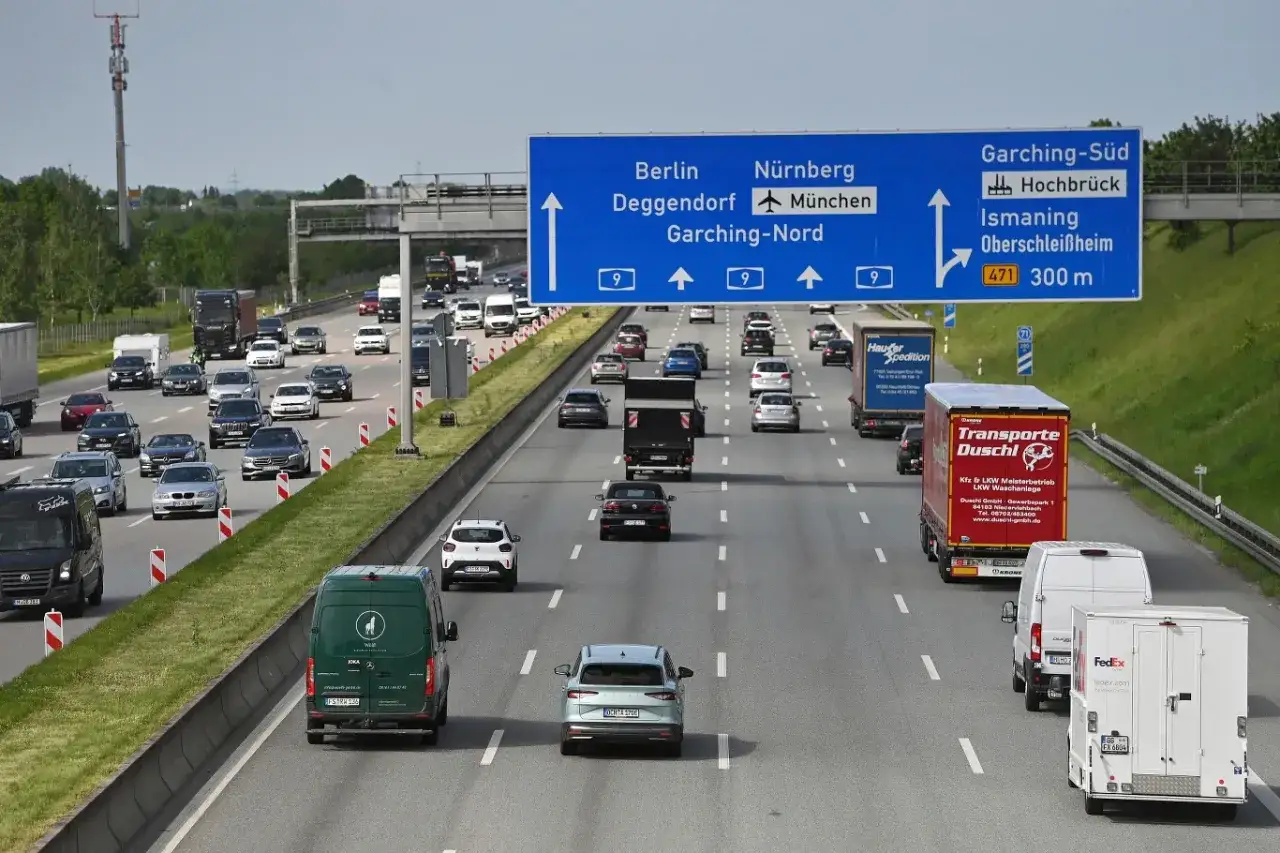 Ruch na autostradach w Niemczech. Samochody osobowe i ciężarowe jadą wielopasmową drogą, kierując się zgodnie ze znakiem na Berlin, Norymbergę i Monachium.
