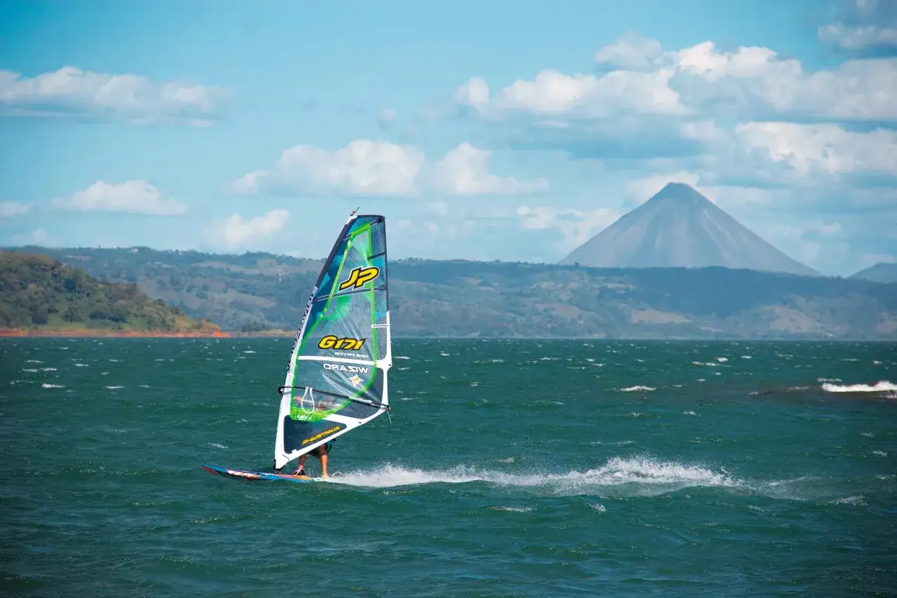 Windsurfer gleitet über den Arenal See, im Hintergrund der majestätische Vulkan.