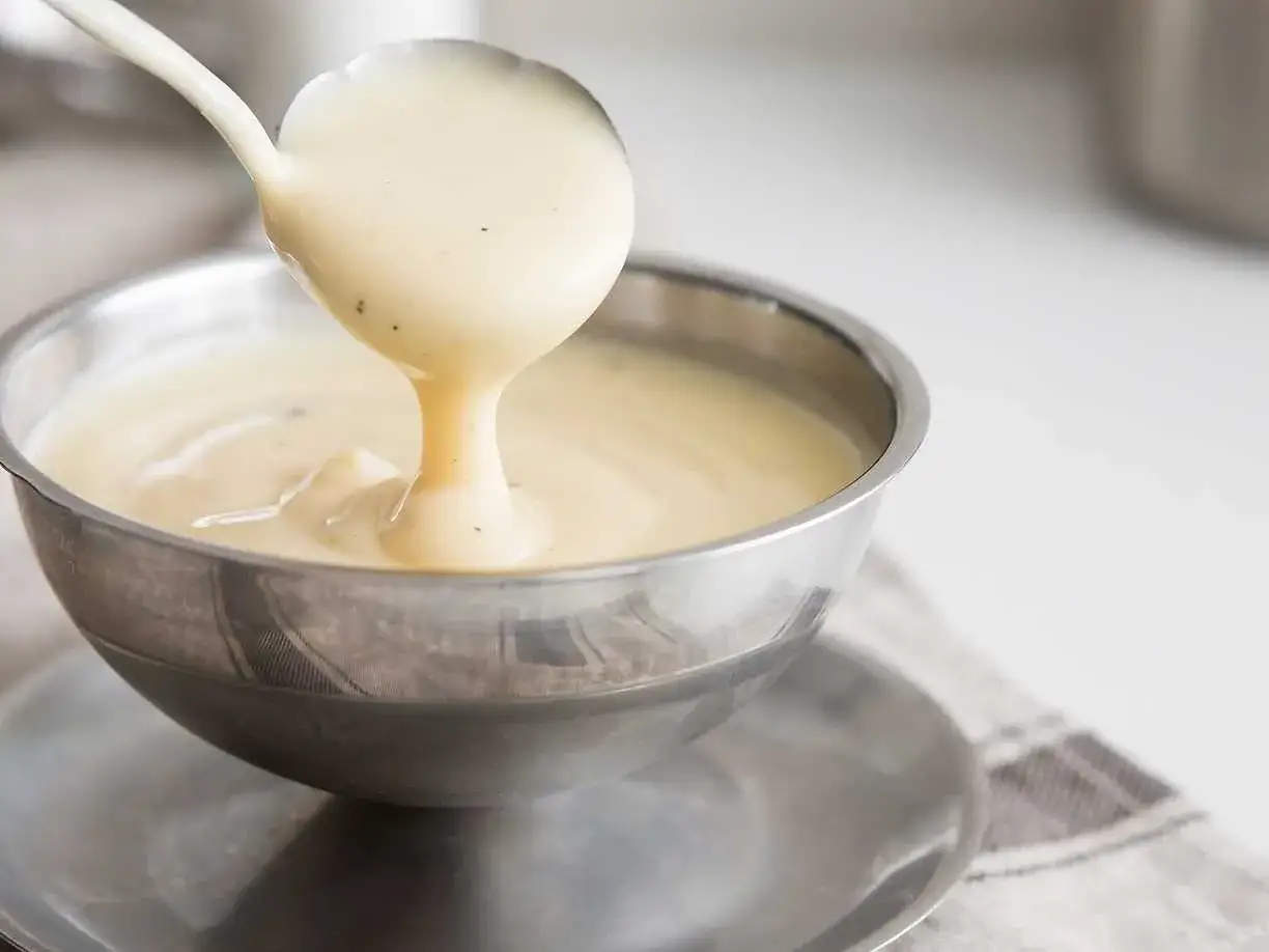 Krämig vaniljsås hälls upp ur en slev i en skål. Perfekt för ditt vaniljsås recept!