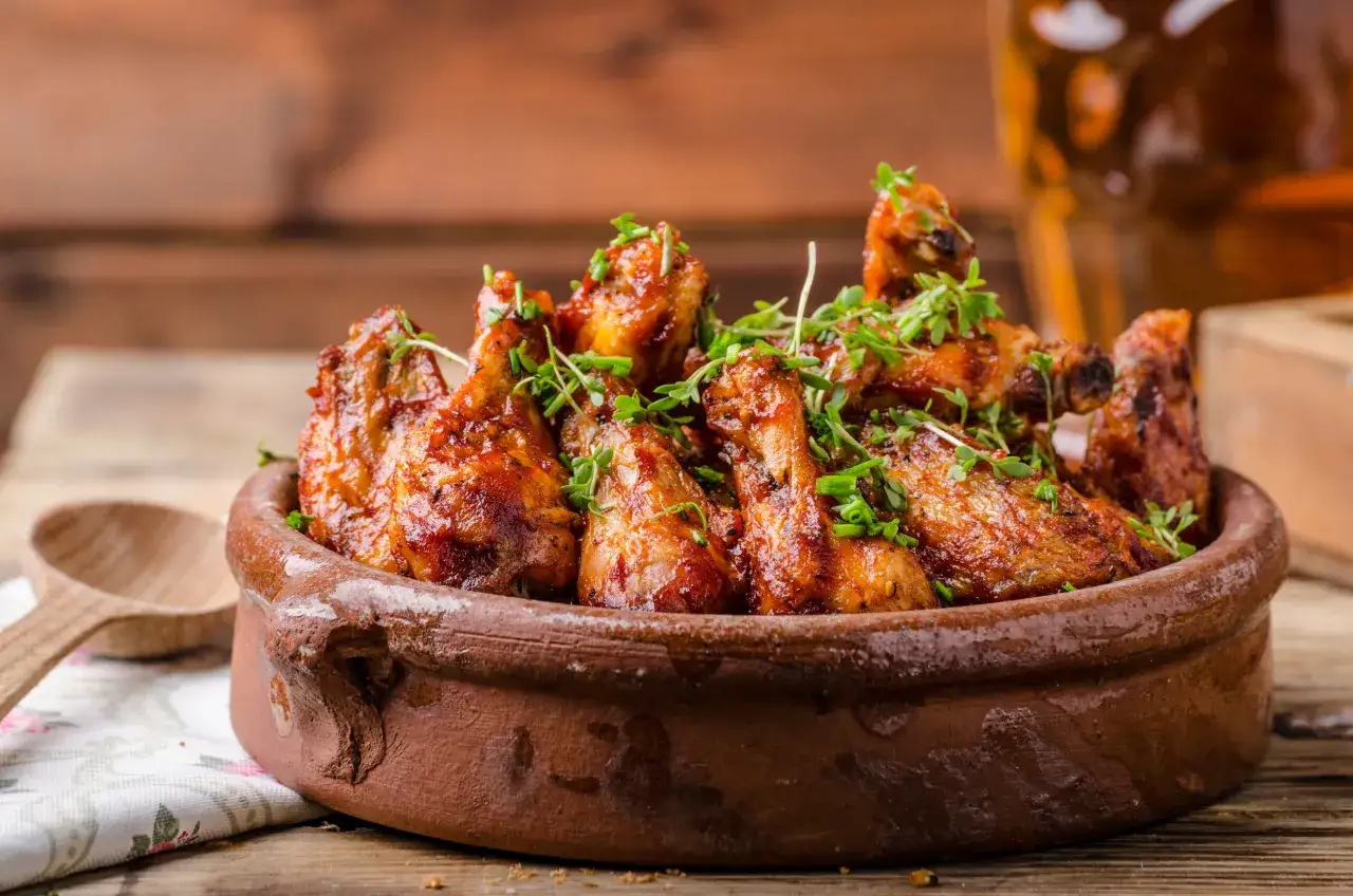 Chrupiące skrzydełka z kurczaka w sosie BBQ, podane w glinianej misie. Idealne na grilla lub do pieczenia.
