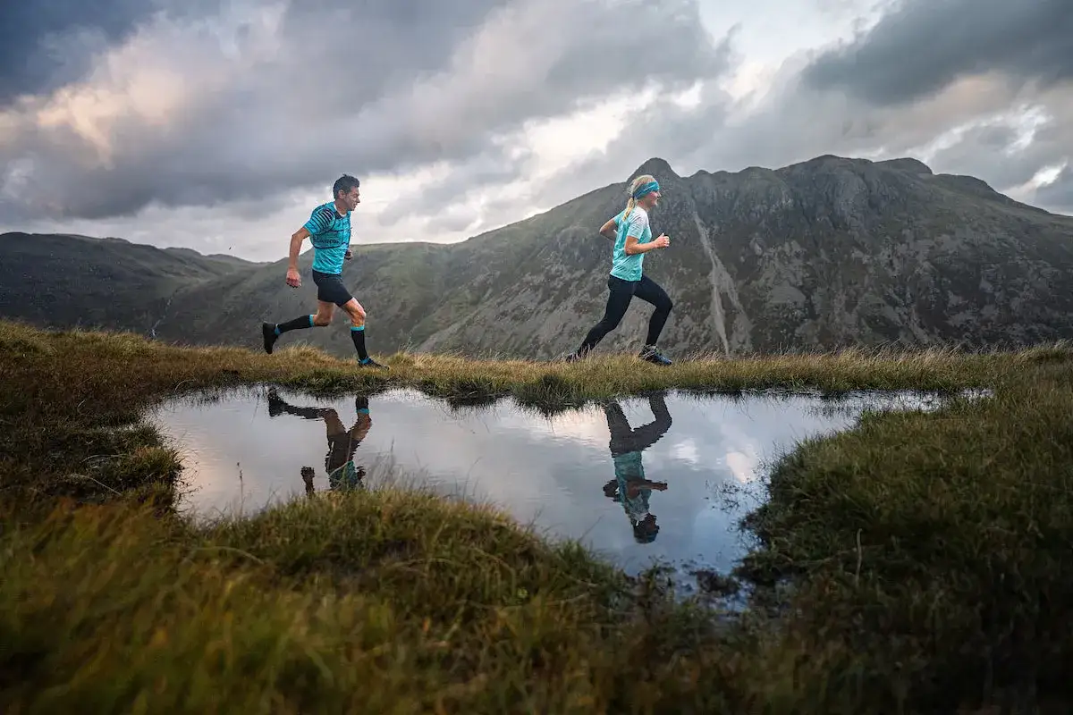 Deux coureurs profitent des bienfaits de la course à pied en pleine nature, leurs reflets dans l'eau reflétant la beauté du paysage montagneux.