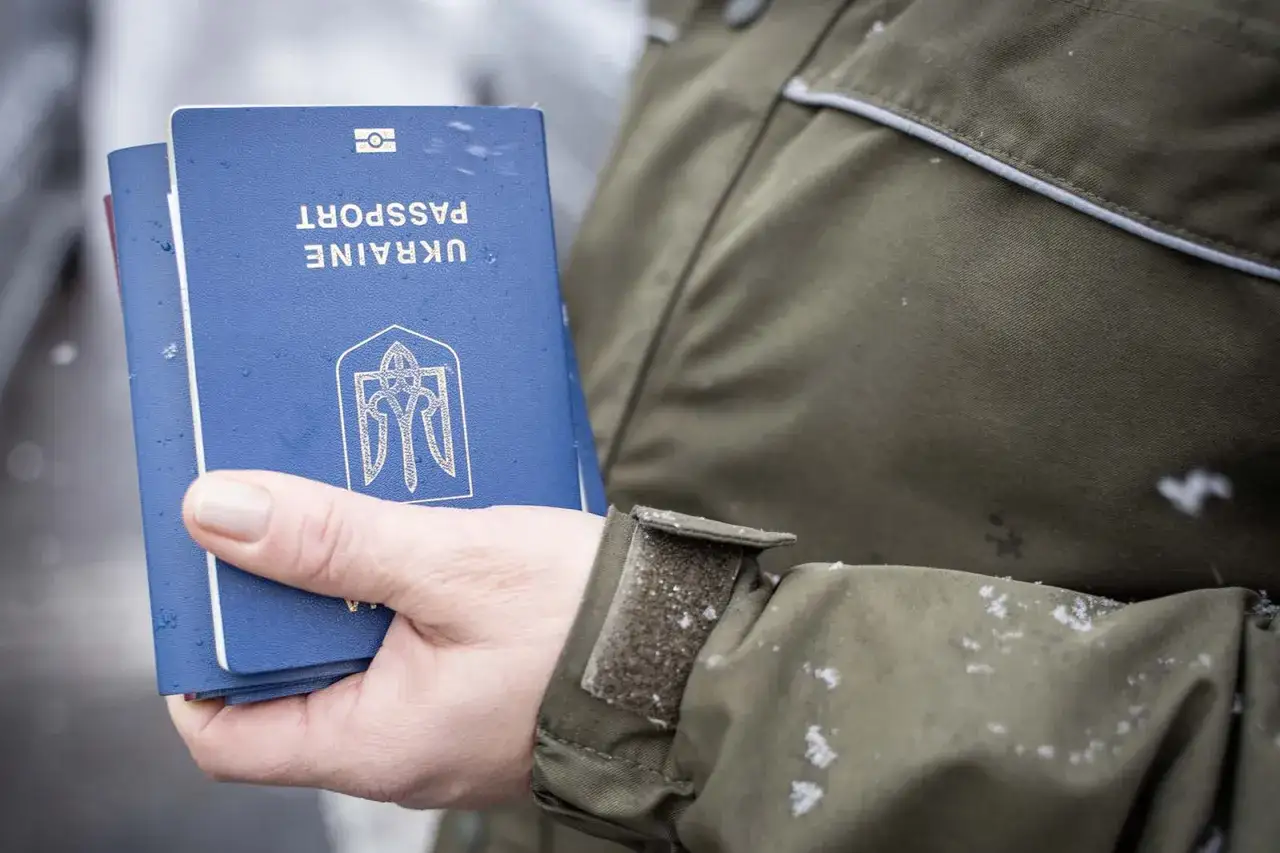 Dłoń trzyma paszporty Ukrainy. W tle widać mundur osoby, która przeprowadza kontrolę graniczną.