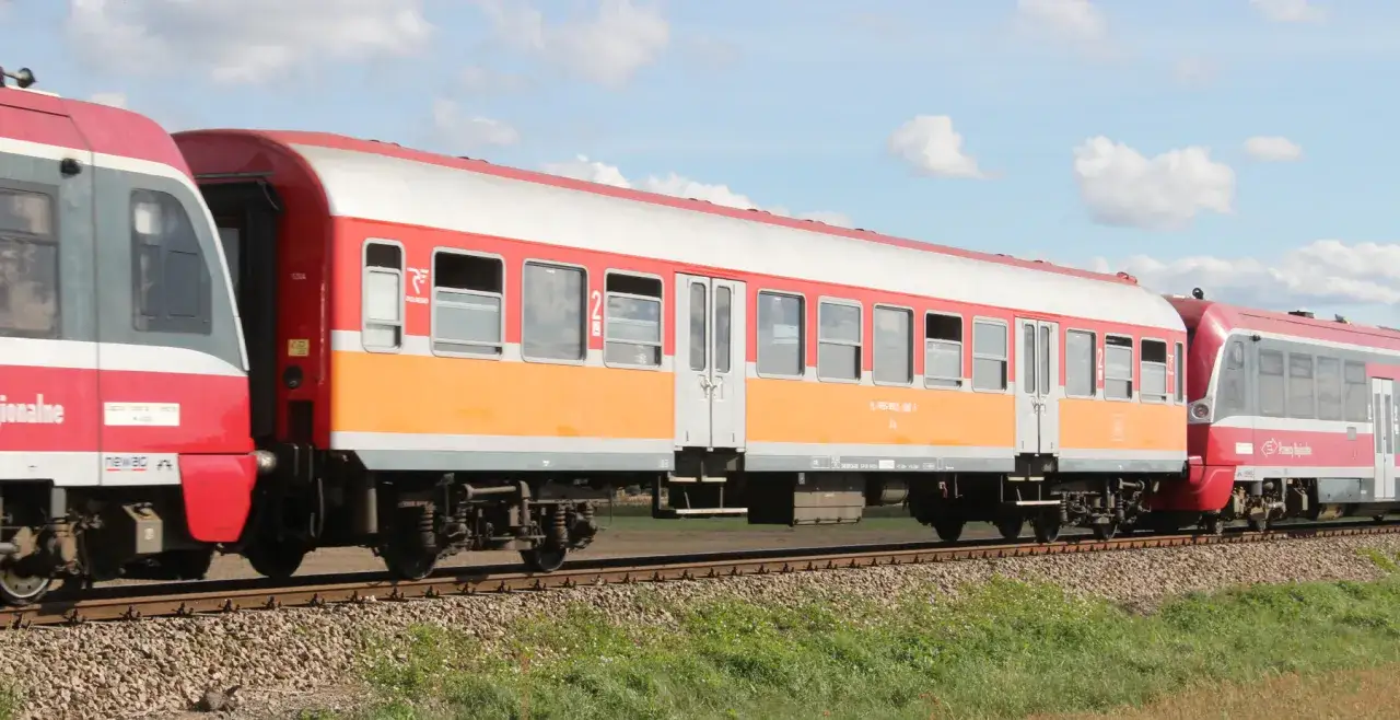 Czerwono-pomarańczowy, lekki wagon pasażerski jedzie po torach.