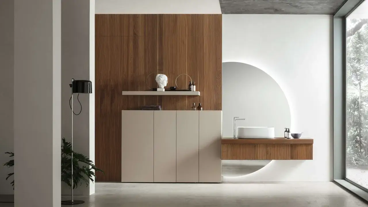 Bagni belli con mobile sospeso in legno, lavabo bianco e specchio circolare retroilluminato.