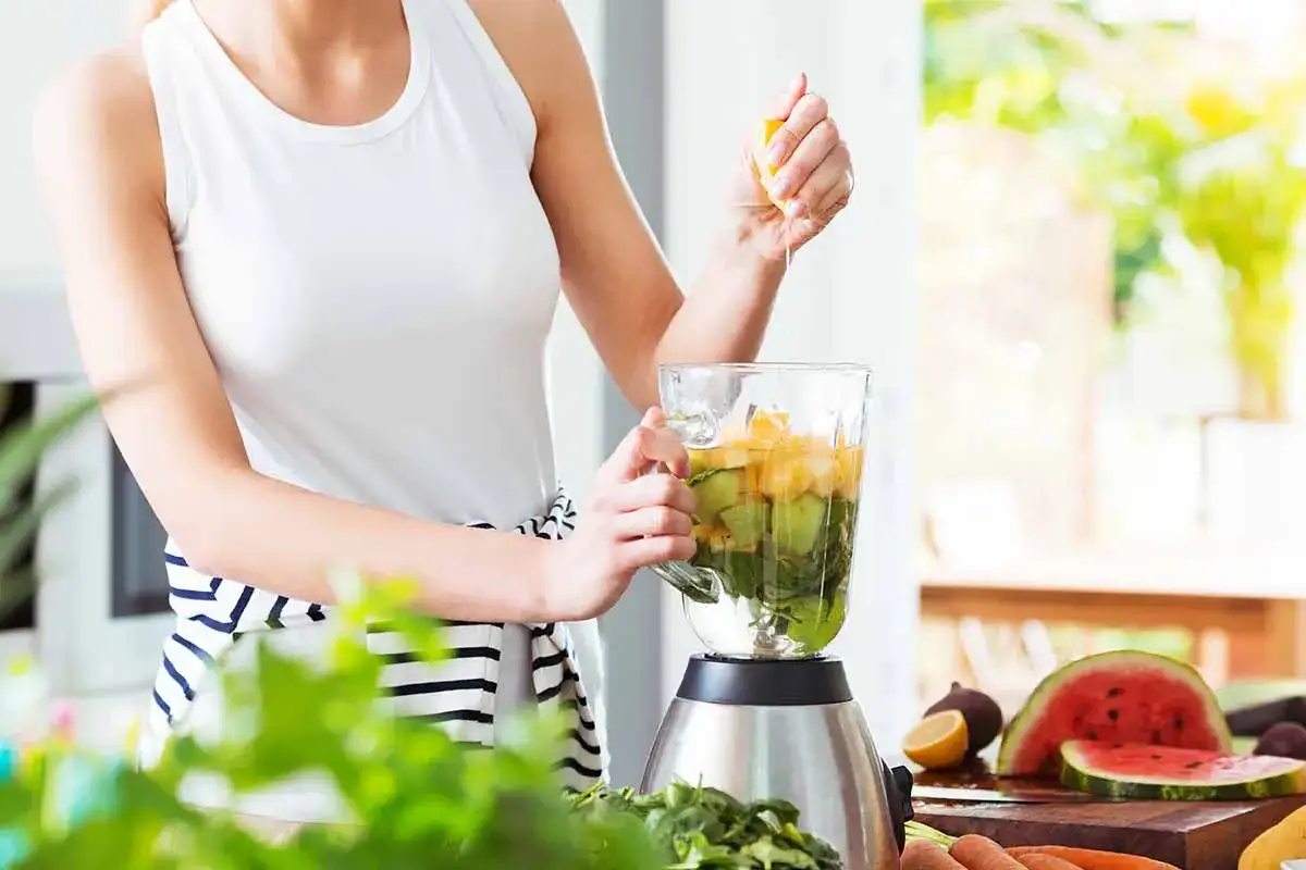 Kobieta dodaje cytrynę do blendera z owocami i warzywami, przygotowując pyszny smoothie.