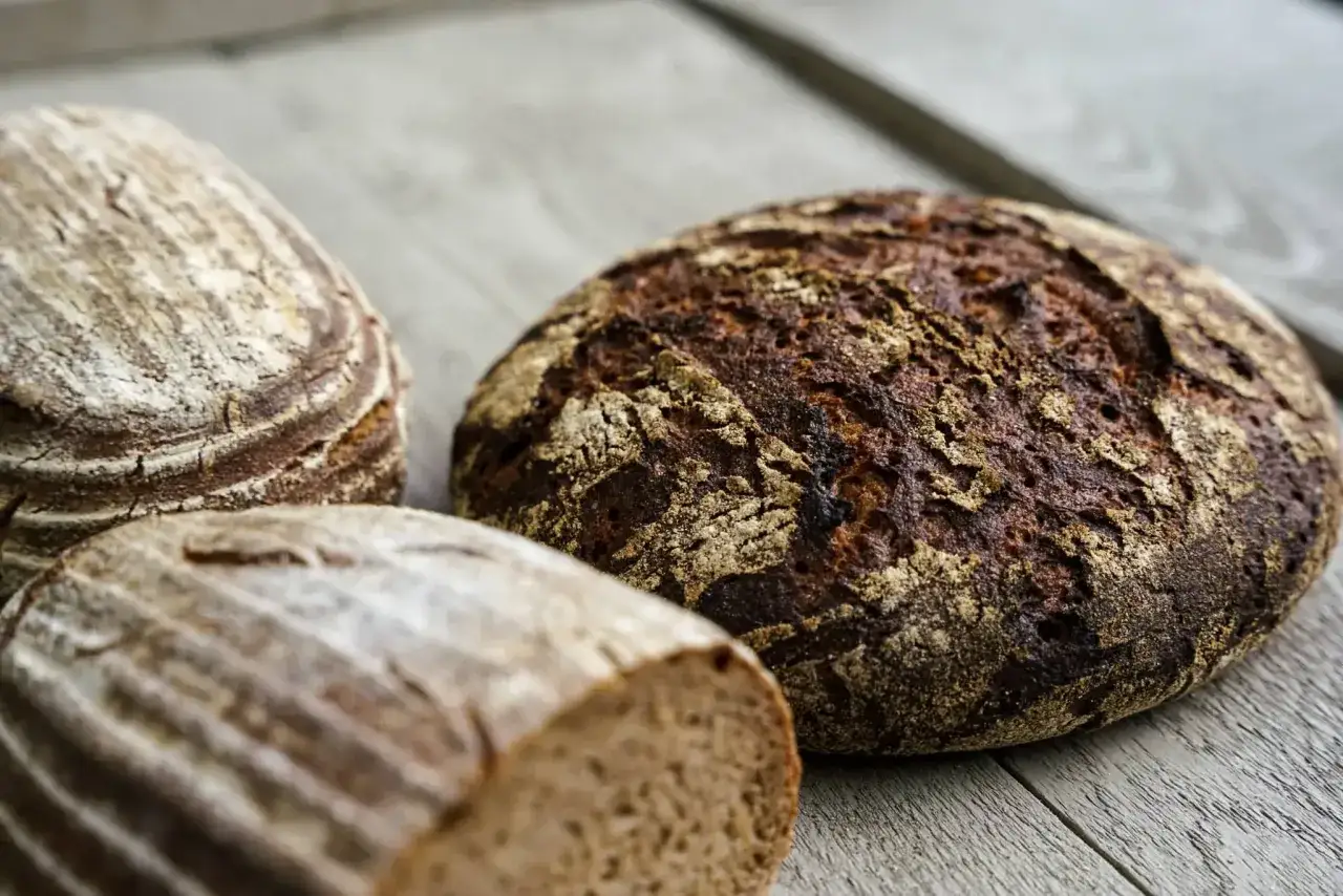 Drei rustikale Roggenbrote liegen auf einem Holztisch. Sie zeigen, was man aus Roggen machen kann: herzhaftes Brot.