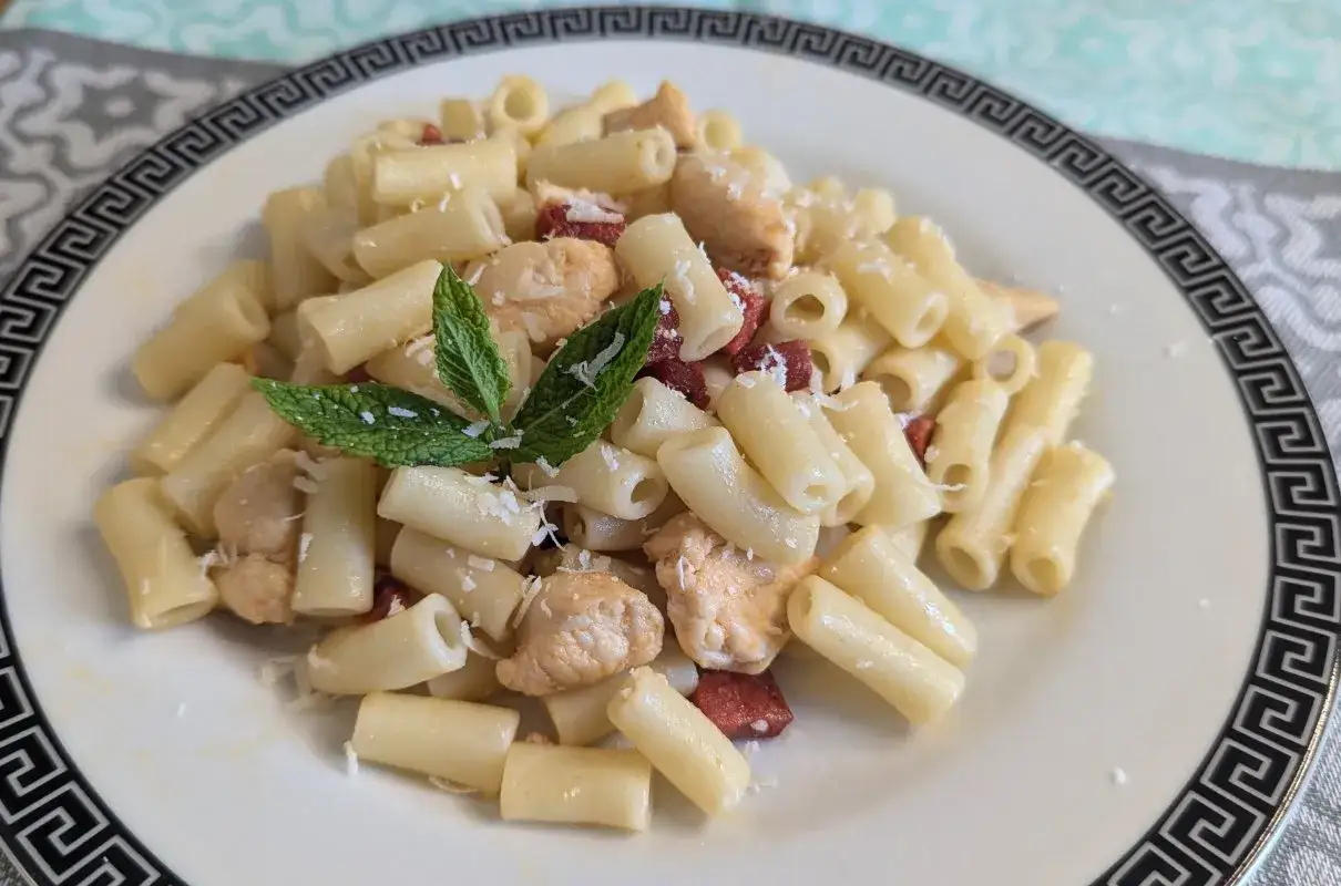 Pyszny makaron z kawałkami kurczaka i pikantnym chorizo, posypany parmezanem i udekorowany listkami mięty.