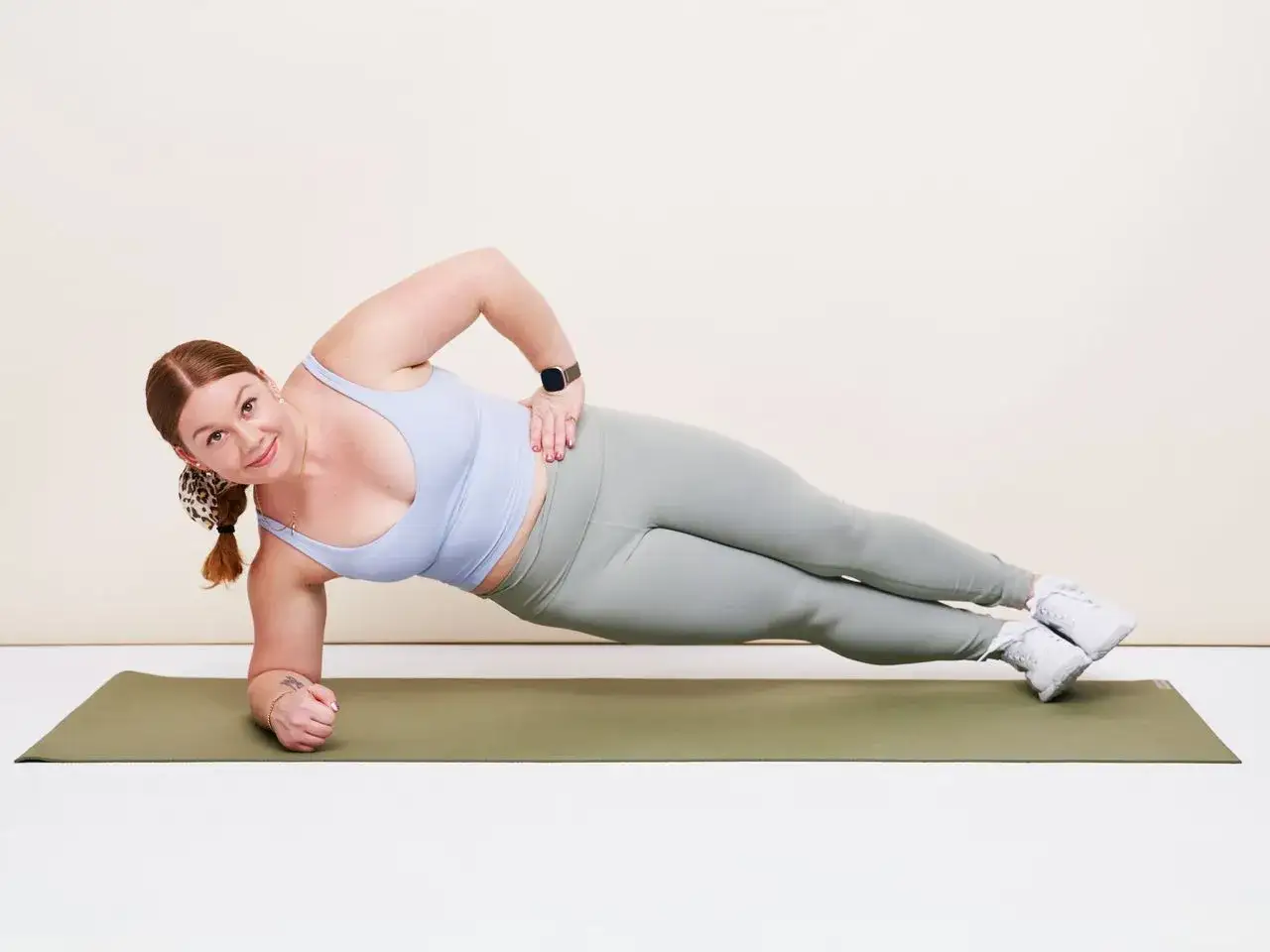 Femme souriante en position de planche latérale, un exercice pour apprendre comment faire des abdos.