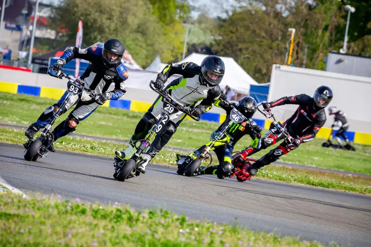 Des pilotes en combinaison s'affrontent dans une course de trottinette électrique sur un circuit.