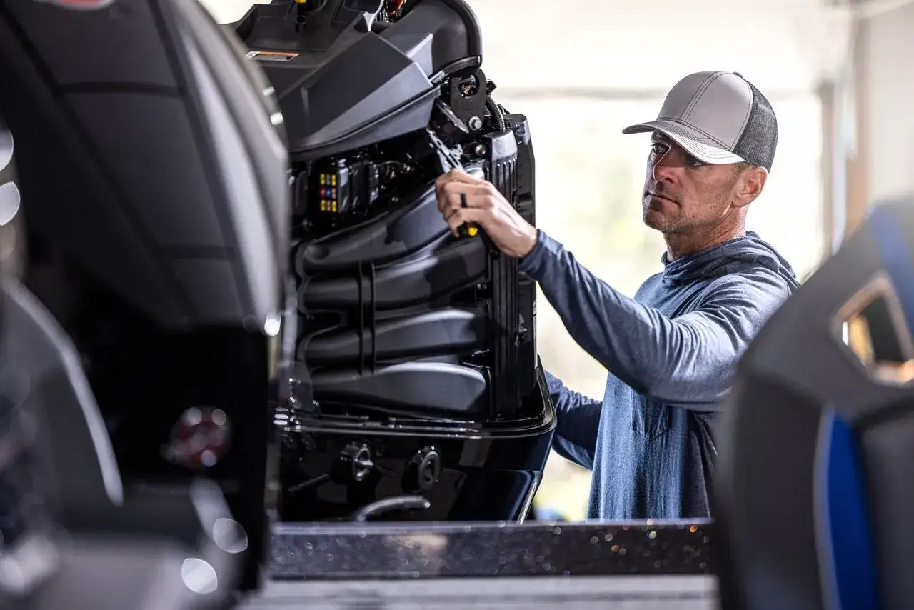 Un homme prépare son moteur hors bord pour l'hivernage, vérifiant les composants avec une clé.