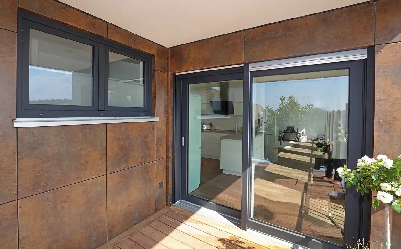 Ventanas de PVC de color gris oscuro en una fachada moderna. Reflejan el cielo y el interior de una cocina luminosa.