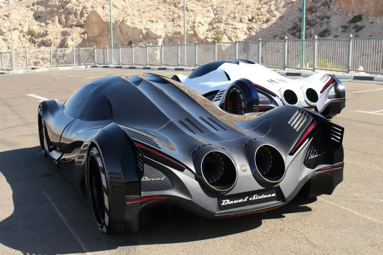 Dwa futurystyczne samochody Devel Sixteen, jeden czarny, drugi biały, stoją na parkingu.