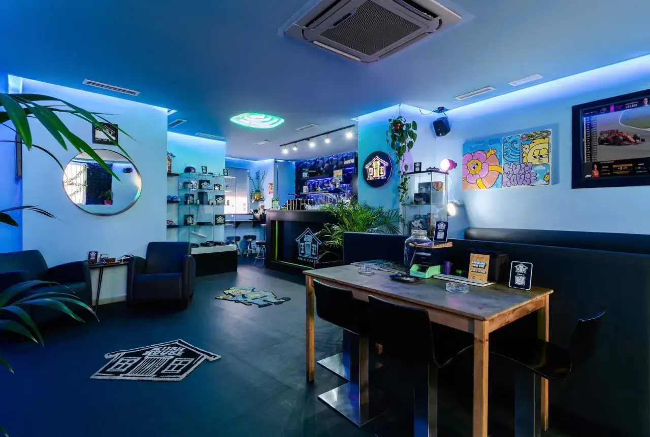 Interno di un social club a Barcellona, con illuminazione blu, arredi moderni e opere d'arte colorate.