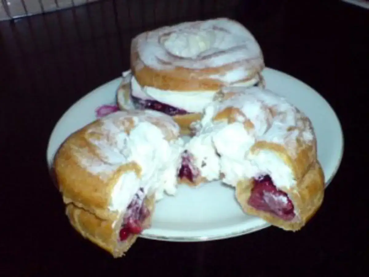Zwei Windbeutel mit Kirschen und Sahne, best&auml;ubt mit Puderzucker, auf einem Teller.