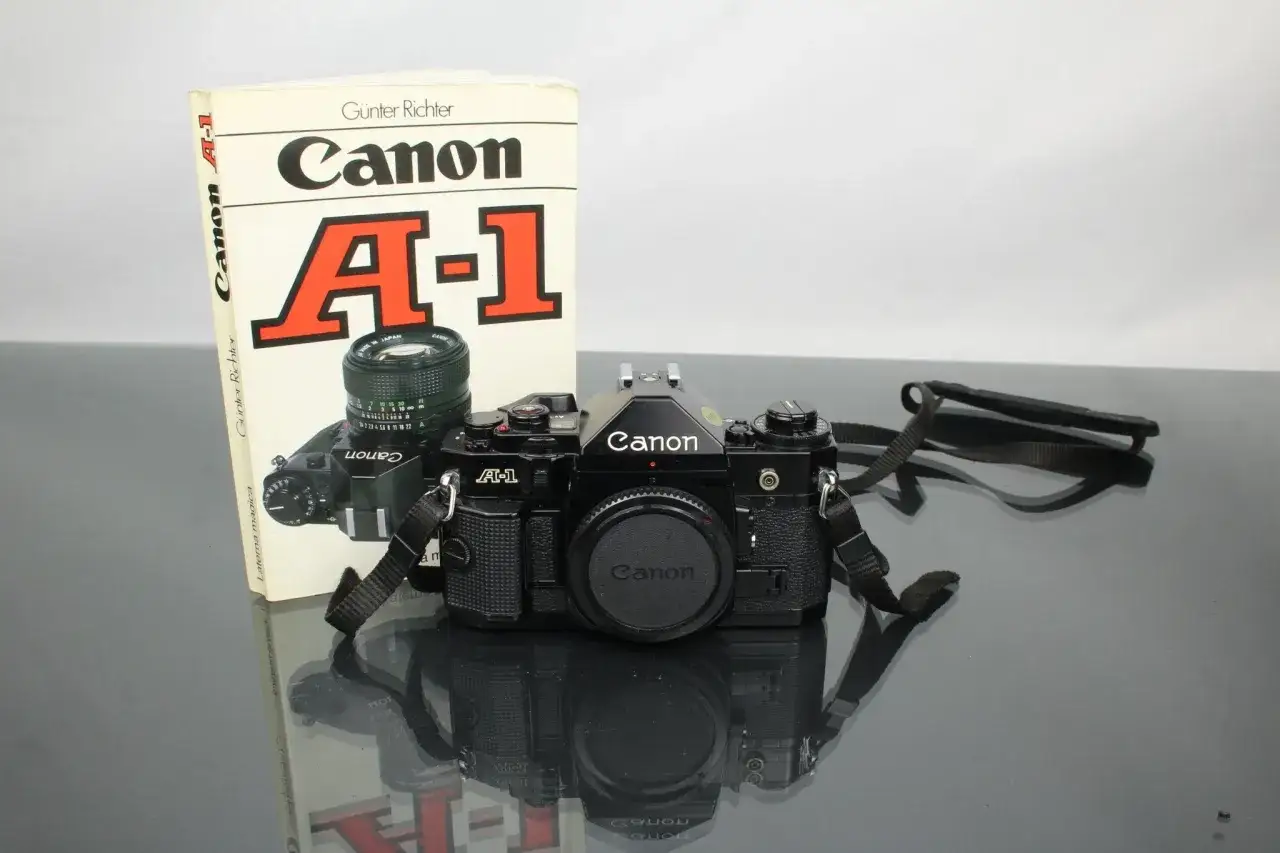 En svart Canon A-1 systemkamera med objektiv och en bok om kameran. En klassiker för den som vill lära sig fotografera.