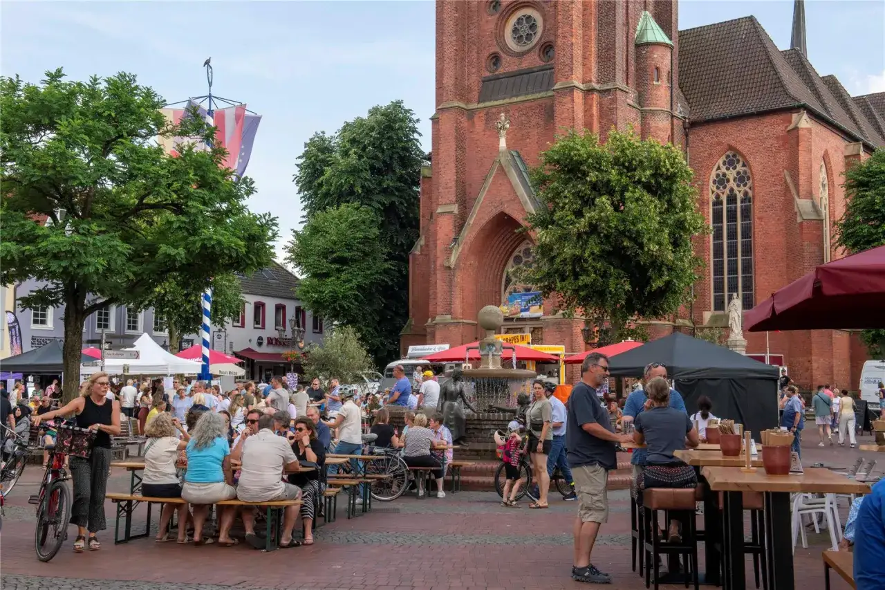 Menschen genie&szlig;en den feierabendmarkt heute vor einer Kirche. Viele sitzen an Tischen, essen und trinken.