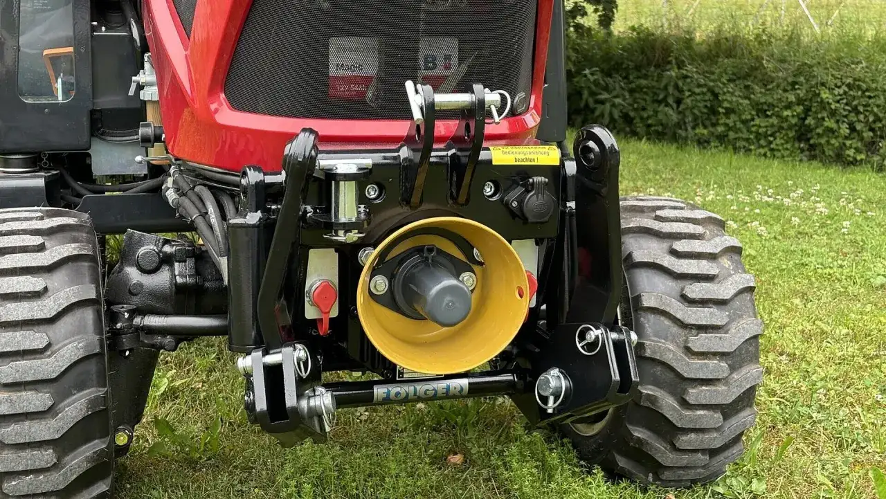 Traktor mit gelbem, weistem dreieckf&ouml;rmigem Anbauger&auml;t und schwarzer Folger-Deichsel.