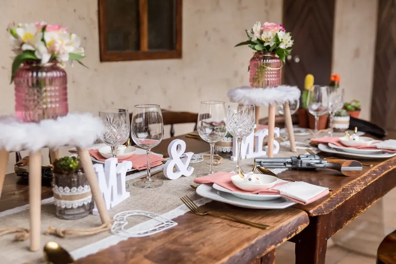 Table dressée pour un mariage western : verres, fleurs roses, et un pistolet décoratif.