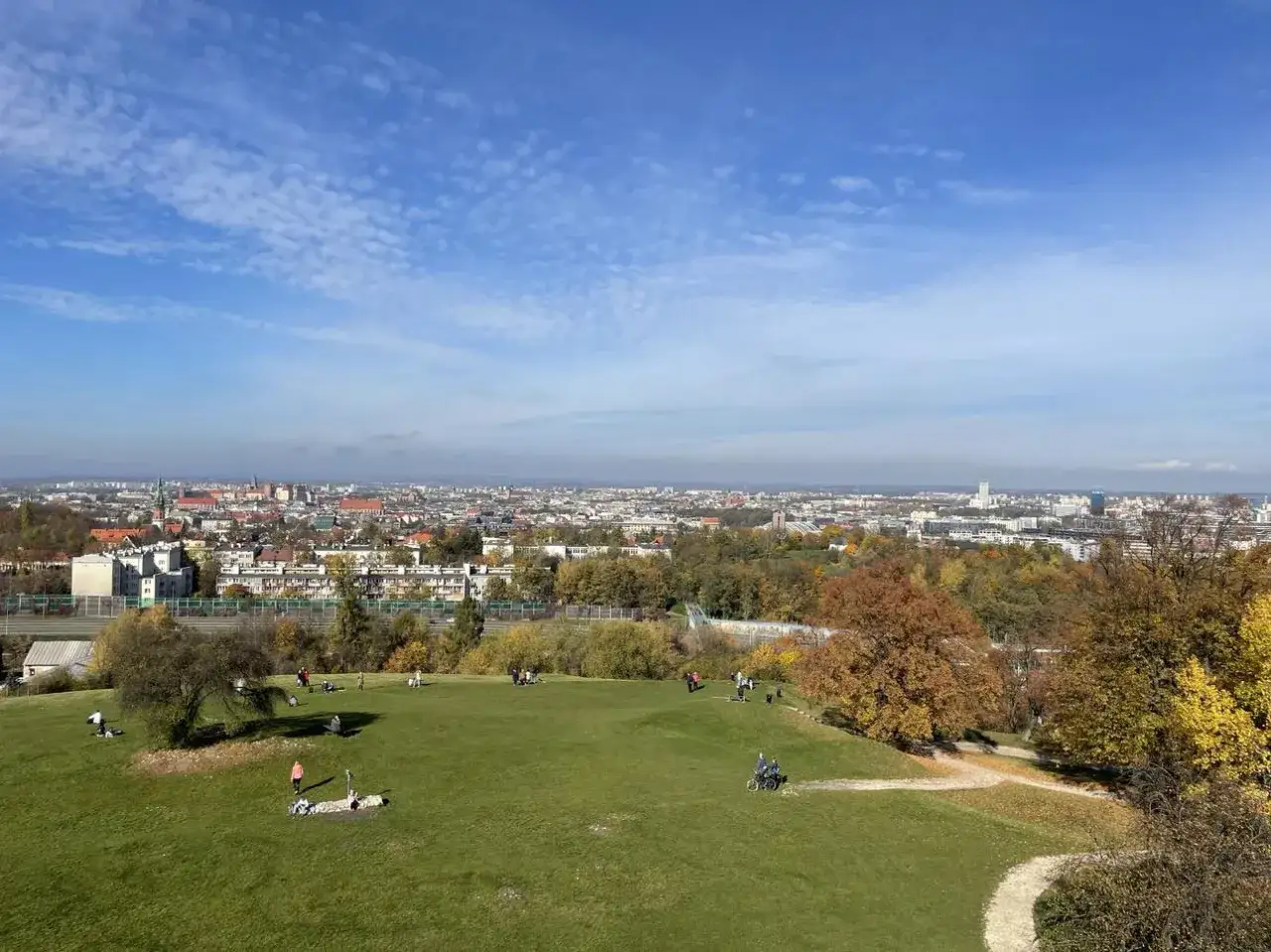 Jesień na Kopcu Kraka. Ludzie odpoczywają na zielonej trawie, w tle rozciąga się panorama Krakowa.