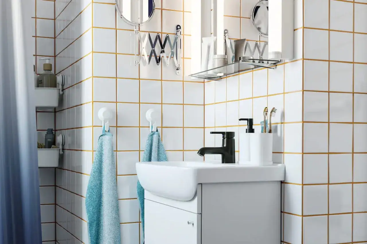 Salle de bain moderne avec carrelage blanc et joint carrelage couleur or. Lavabo, robinetterie noire, porte-serviettes et accessoires.