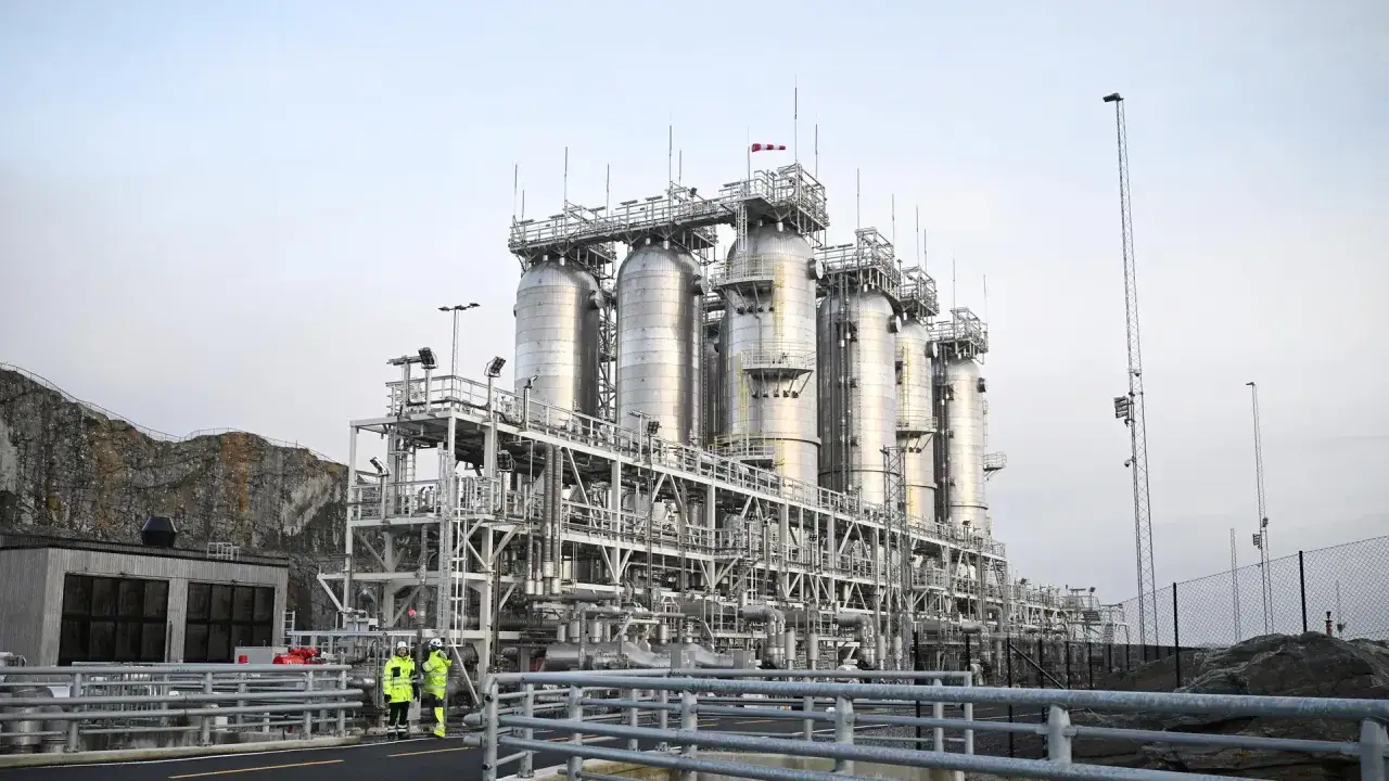 Industrielle Anlage mit gro&szlig;en Tanks und Rohrleitungen, Teil einer carbon management strategie. Zwei Personen in Warnwesten inspizieren das Gel&auml;nde.