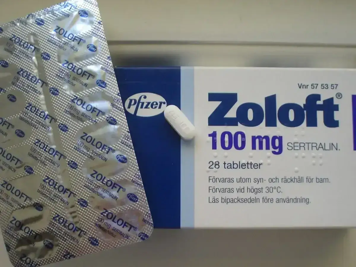 Opakowanie leku Zoloft 100 mg z sertraliną, obok blister z tabletkami.