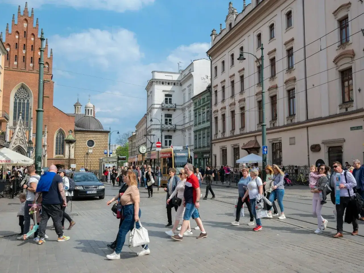 Ludzie spacerują po Rynku Głównym w Krakowie. Czy 1 maja jest dniem wolnym od pracy? Widać tramwaj i zabytkową architekturę.