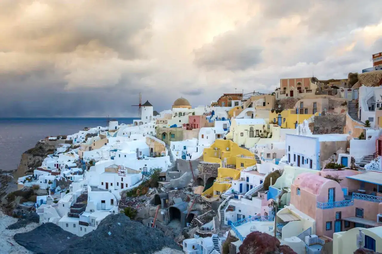 Grecja, grudzień: białe domy na klifie Santorini, wiatraki i morze pod zachmurzonym niebem.
