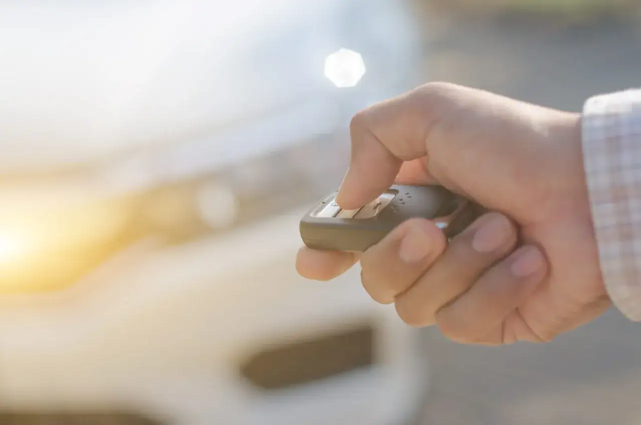 Dłoń trzyma kluczyk samochodowy, naciskając przycisk. To pokazuje, jak działa immobilizer, zabezpieczając auto przed kradzieżą.