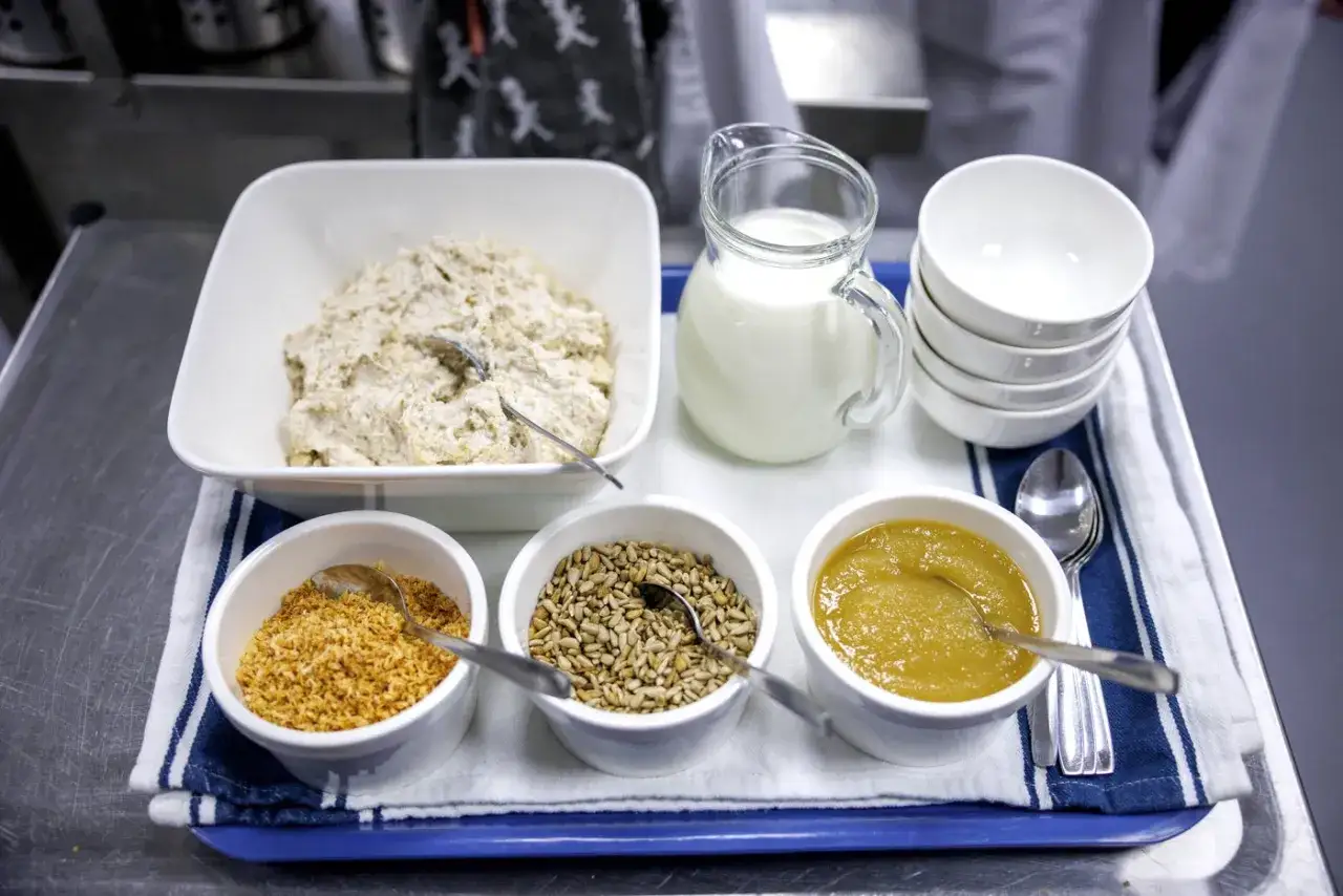 Frukostbricka med ingredienser f&ouml;r overnight oats: havregryn, mj&ouml;lk, &auml;ppelmos, solrosfr&ouml;n och rostad kokos.