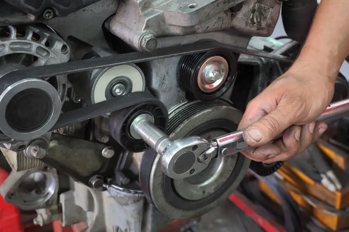 Mécanicien ajustant la courroie d'accessoires d'un moteur. Le bruit poulie damper est peut-être la cause du problème.