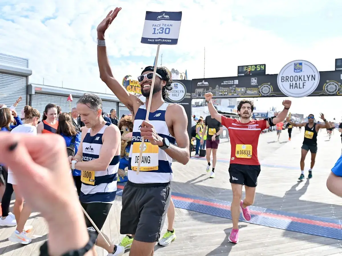 Corridori festeggiano al traguardo della Brooklyn Half. Un uomo con cartello 