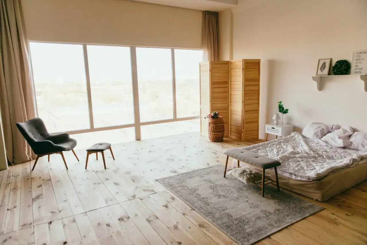 Sypialnia z dużym oknem, łóżkiem i fotelem. Drewniana parawan i kosz z kwiatami dodają uroku, tworząc harmonię w stylu feng shui.