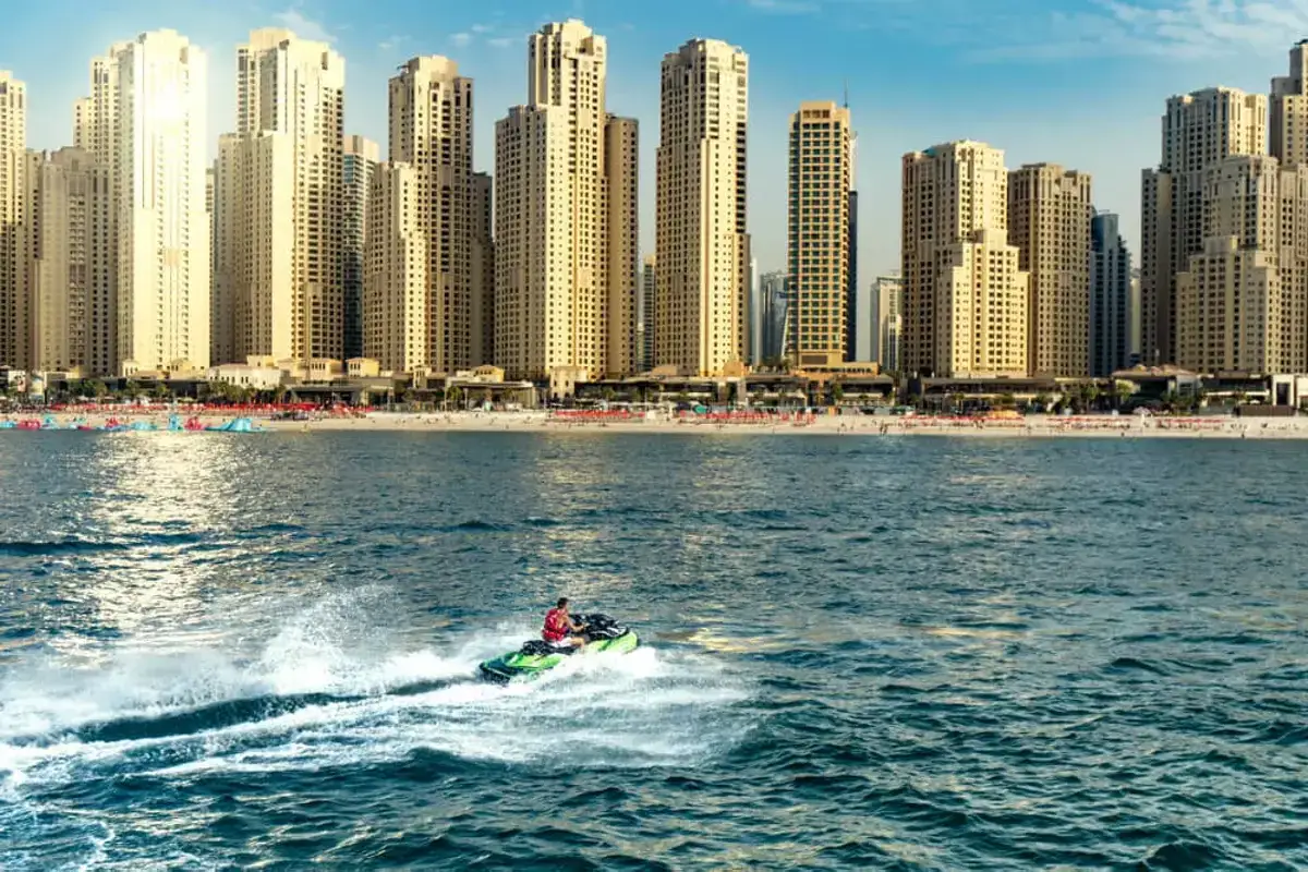 Osoba na skuterze wodnym śmiga po falach przed imponującą panoramą drapaczy chmur na plaży w Dubaju.