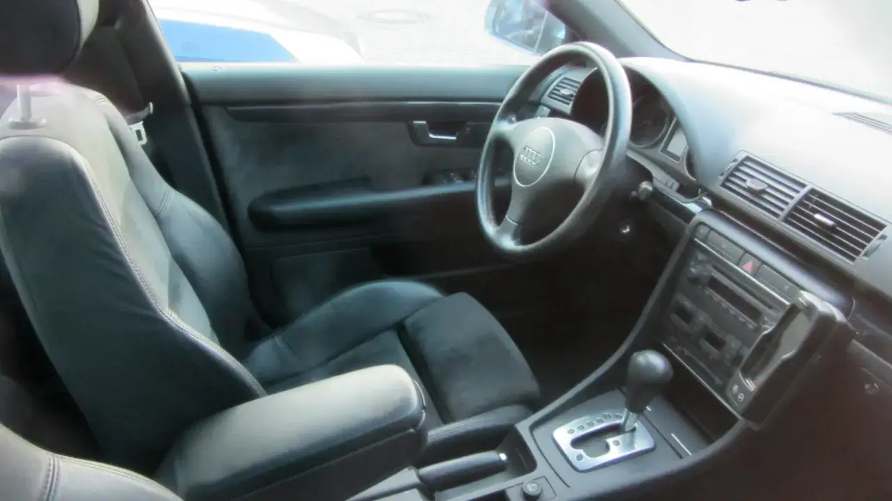 Wnętrze Audi B6 z czarną, skórzaną tapicerką i sportowymi fotelami. Widoczna kierownica, deska rozdzielcza i konsola środkowa.