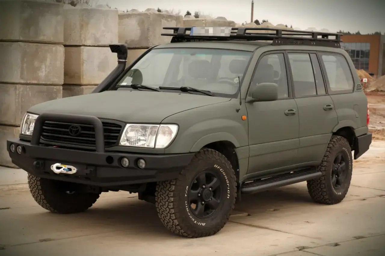 Zielony Land Cruiser 100 z wyciągarką i bagażnikiem dachowym gotowy na przygodę.