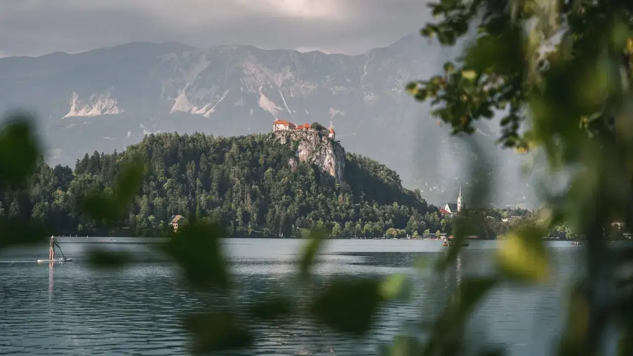 Zamek na skale nad jeziorem, otoczony lasem, to jedno z najpiękniejszych miejsc w Słowenii. W oddali g&oacute;ry i miasteczko.