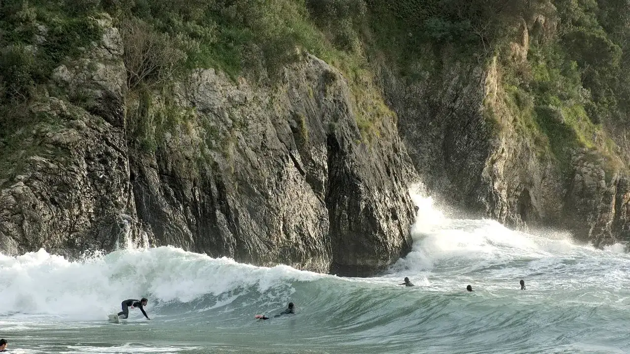 Surfer reitet eine Welle vor steiler Felswand. Mehrere Surfer im Wasser, die die Wellen genie&szlig;en. Rhodos Surfen ist ein aufregendes Erlebnis.