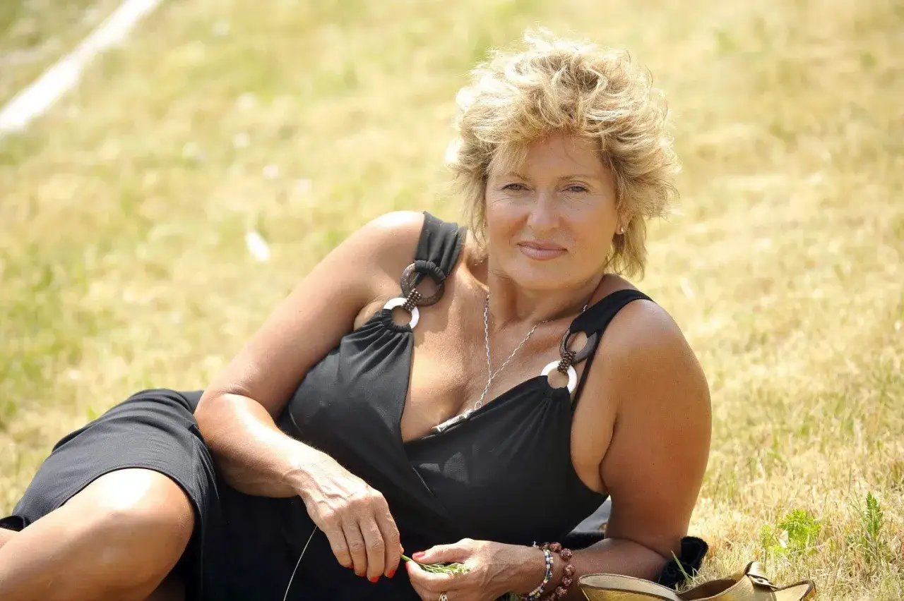 Ewa Kasprzyk, ile ma lat? Aktorka w czarnej sukience leży na trawie, uśmiechając się do obiektywu.
