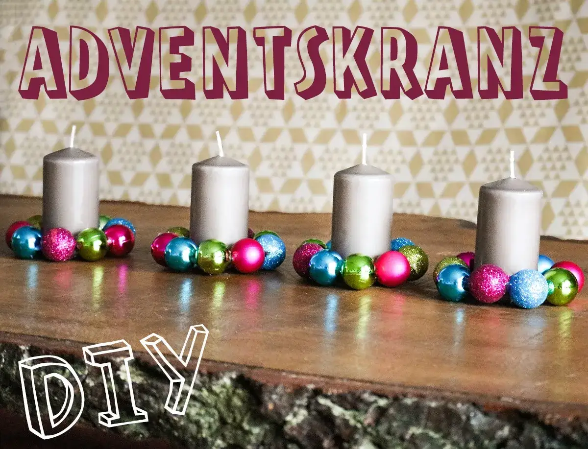 Adventskranz aus Kugeln selber basteln: Vier graue Kerzen auf einem Holzstamm, umgeben von bunten Weihnachtskugeln. DIY-Idee f&uuml;r Weihnachten.