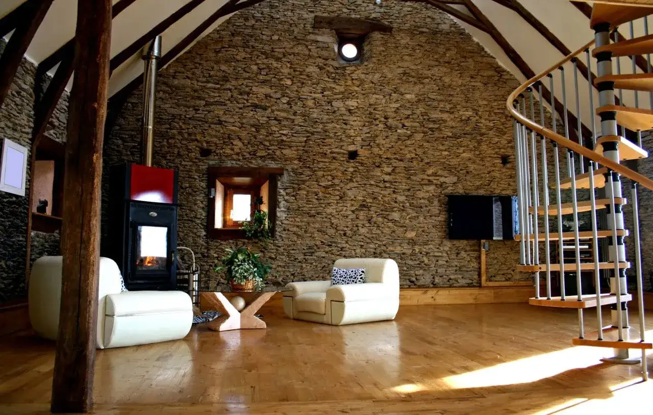 Aménagement intérieur d'une grange rénovée de 100m2 : poêle, fauteuils blancs, escalier hélicoïdal. Le coût rénovation grange 100m2 est un investissement.