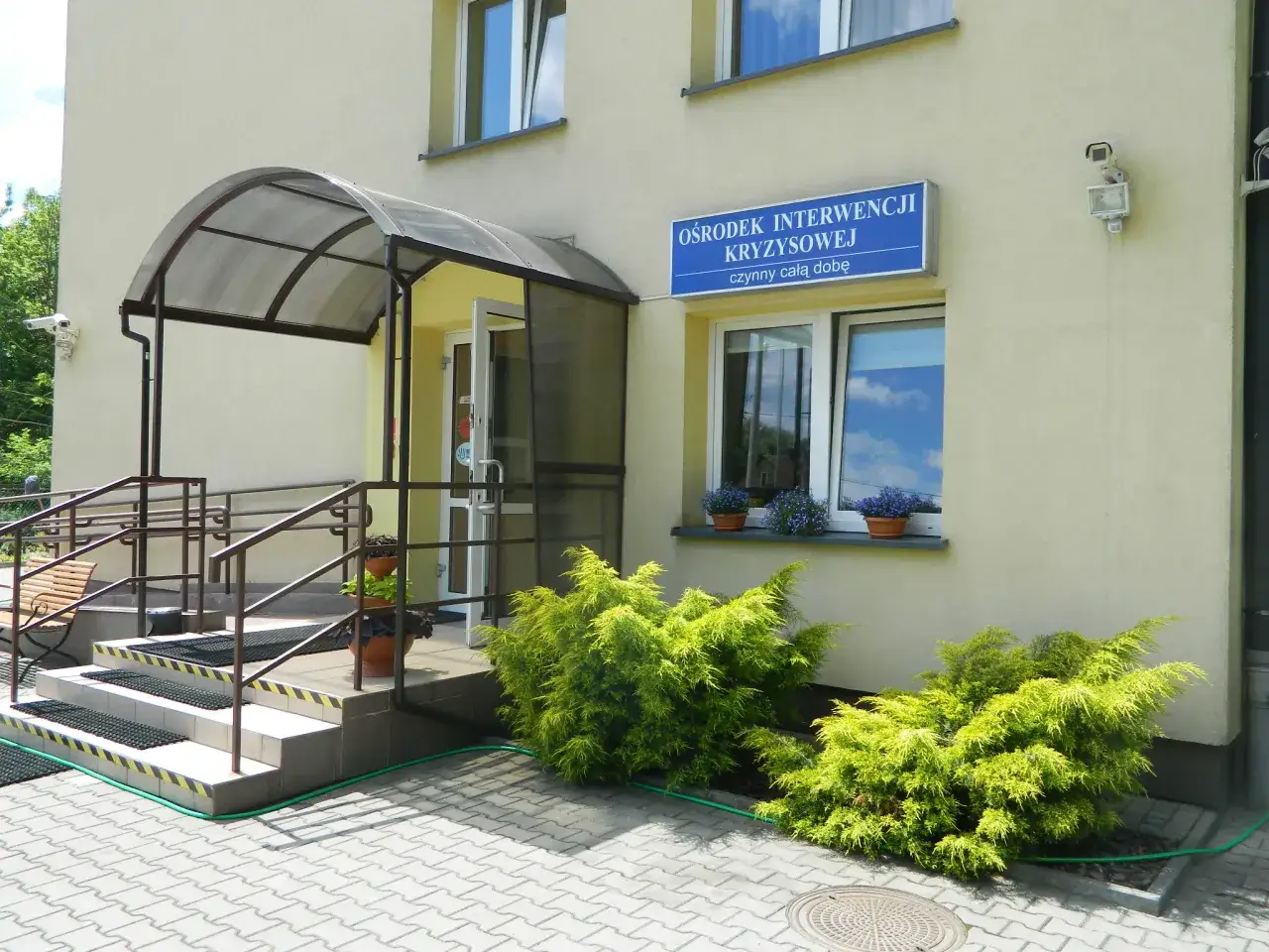 Ośrodek Interwencji Kryzysowej, z zielenią przed wejściem i schodami.